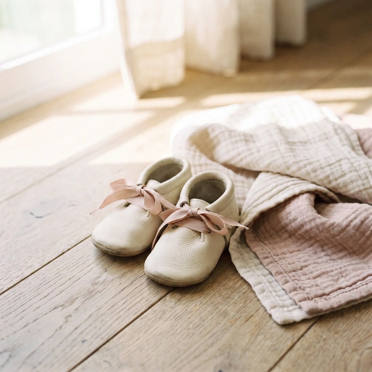 Tiny soft-soled baby shoes beside a folded muslin blanket